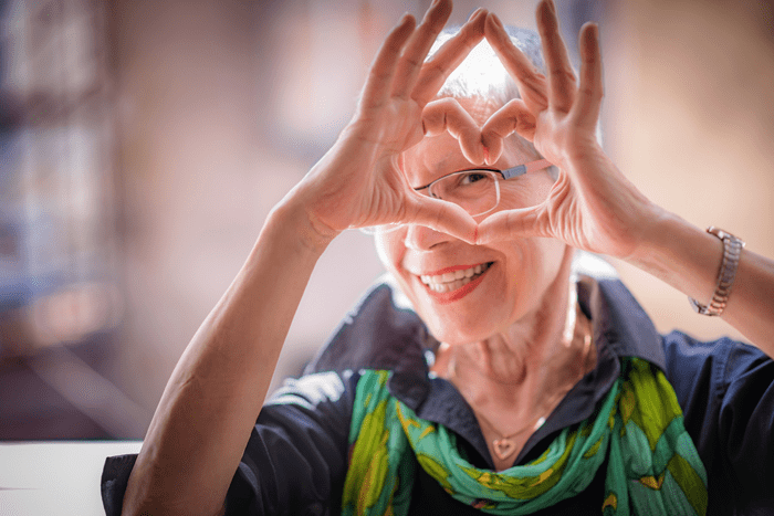 Senior Woman holding up heart shape with hands.